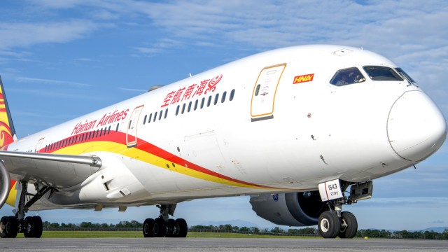 Hainan Airlines aircraft on the airport tarmac under a blue sky.