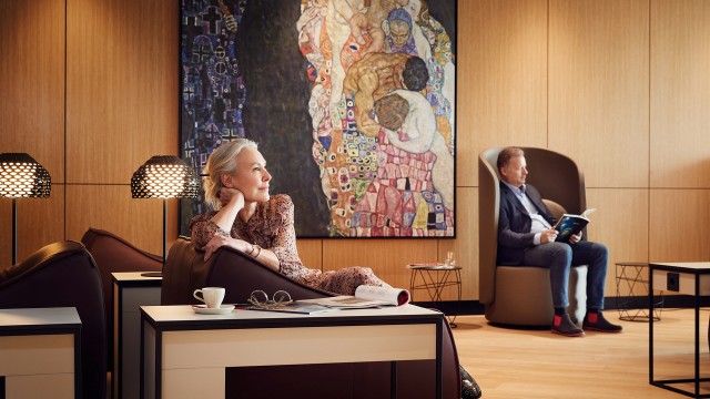 Eine blonde Frau sitzt in der Vienna Lounge vor einem Klimt Gemälde.