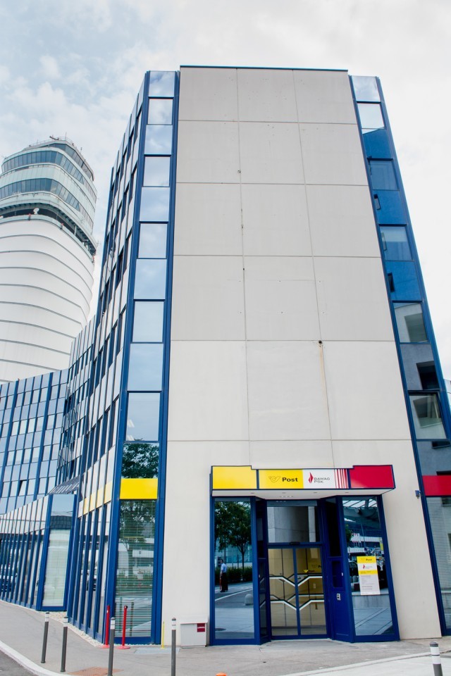 Postfiliale im modernen Gebäude am Flughafen mit dem Tower im Hintergrund.