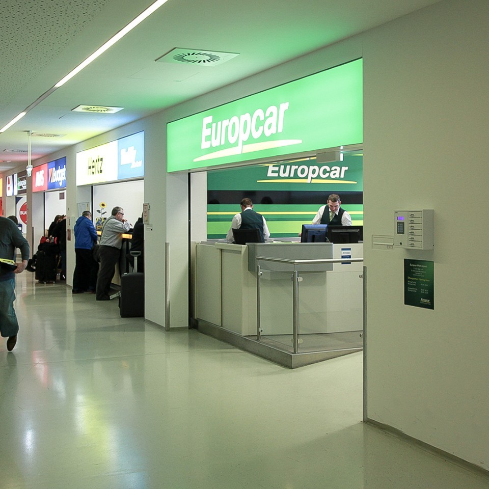 Schalterbereich mehrerer Autovermietungen am Flughafen, darunter Europcar, Hertz und Avis.
