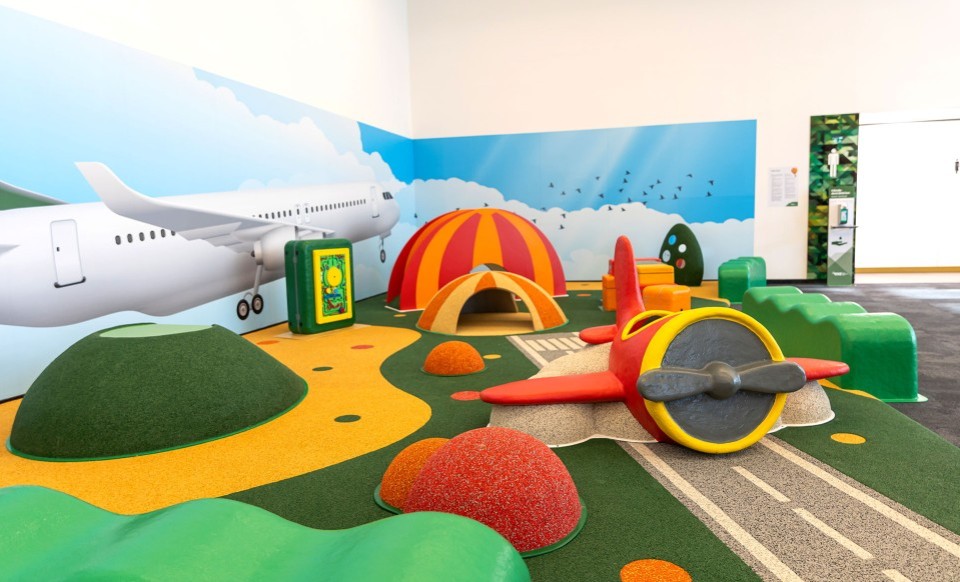 Spielbereich mit Flugzeugthema für Kinder, bunte Hügel, Tunnel und ein rotes Spielzeugflugzeug.
