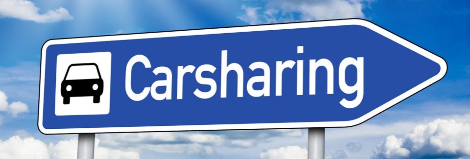 Blaues Verkehrsschild mit weißem Auto-Symbol und der Aufschrift „Carsharing“ vor blauem Himmel.