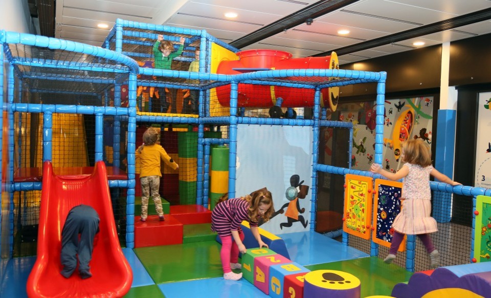 Kinder spielen in einem bunten Indoor-Spielplatz mit Rutsche, Kletterbereich und Bausteinen.