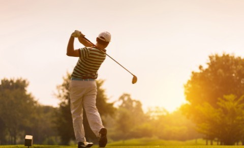 Golfer schlägt den Ball bei Sonnenuntergang auf einem Golfplatz ab.