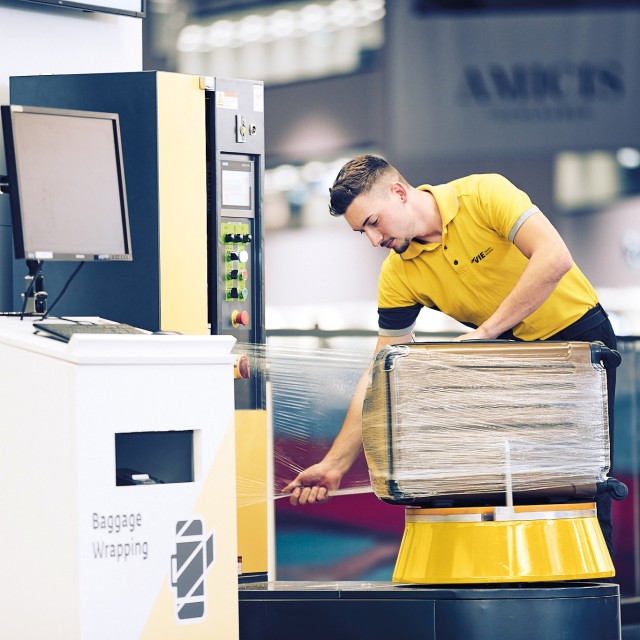 An airport employee wraps luggage in protective plastic film.