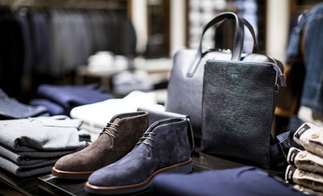 Ein Display in einem Bekleidungsgeschäft zeigt gefaltete Kleidung, zwei Paar Schuhe und eine schwarze Ledertasche.