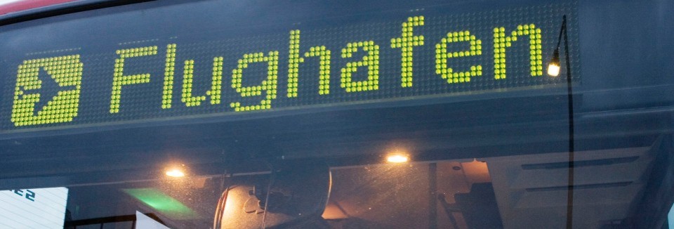 Digitale Anzeige auf einem Bus mit dem Ziel „Flughafen“ und Flugzeugsymbol.