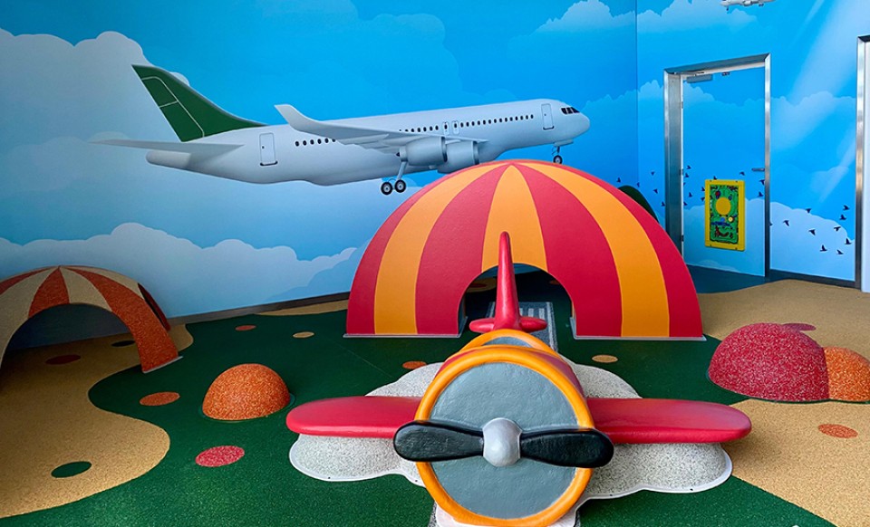 Colorful indoor play area with airplane theme at the airport, featuring toy plane and climbing tunnels.