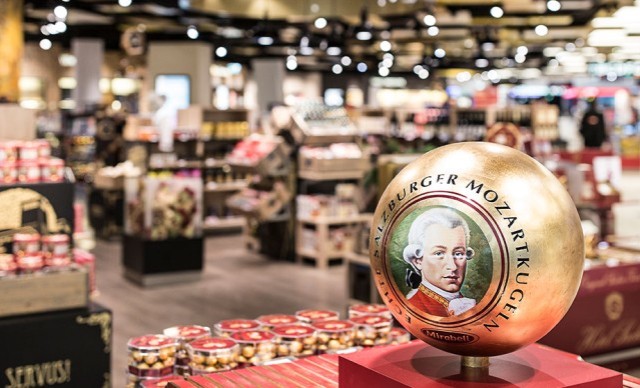 Eine goldene Mozartkugel-Verpackung, umgeben von weiteren Süßigkeiten und Regalen im Hintergrund .