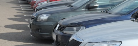 Reihe parkender Autos auf einem Freiluftparkplatz, aufgenommen von der Seite.