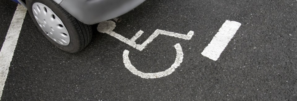 Ein Auto steht teilweise auf einem Behindertenparkplatz, markiert mit dem Rollstuhlsymbol auf dem Asphalt.