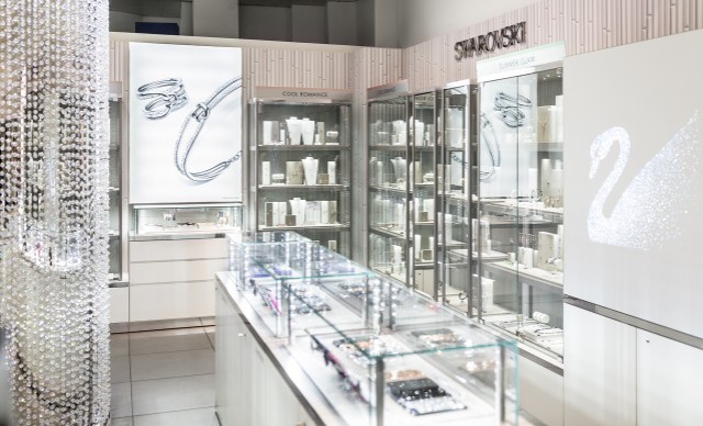 Schmuckgeschäft mit Swarovski-Produkten, beleuchtete Vitrinen mit Schmuckstücken und ein Schwan-Logo an der Wand.