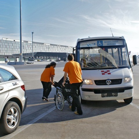 Barrierefrei Reisen: Mitarbeiter des Flugahfen Wien helfen Person mit Rollstuhl