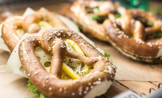 Drei Brezeln mit Käse und Gemüsefüllung auf einem Holzbrett, bestreut mit Sesamkörnern .
