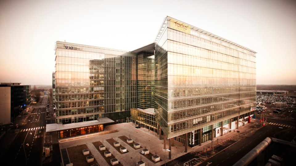 Modernes Bürogebäude mit Glasfassade bei Sonnenuntergang, Blick auf den Innenhof und die Straße, reflektierte Lichtstimmung auf den Fenstern.
