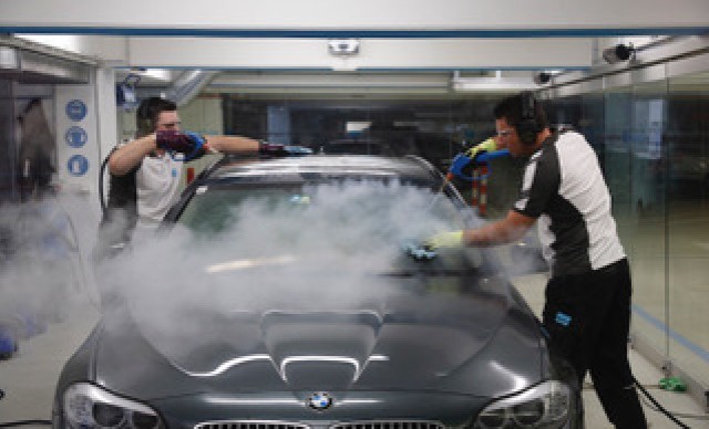 Zwei Mitarbeiter reinigen ein Auto mit Dampfreinigern in einer modernen Autowaschanlage.