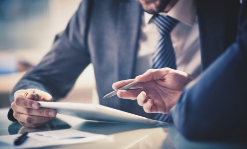 Zwei Männer im Anzug besprechen etwas auf einem Tablet am Schreibtisch.