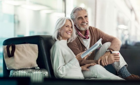 Älteres Paar sitzt entspannt mit Gepäck in einer Flughafenlounge und liest.