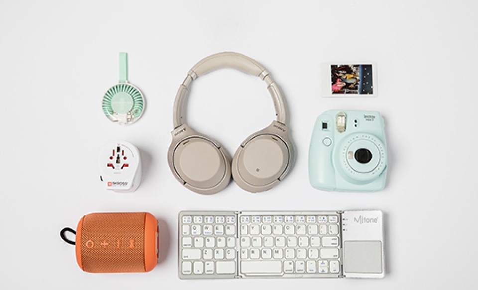 Reisegadgets: Kopfhörer, Sofortbildkamera, Bluetooth-Lautsprecher, Adapter, Mini-Ventilator, faltbare Tastatur und ein Foto.