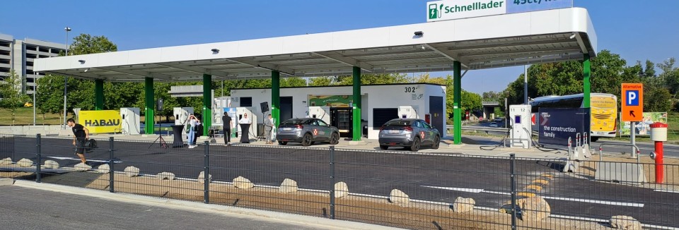E-Tankstelle mit Schnellladern und überdachten Ladeplätzen am Flughafen, mehrere Autos beim Laden.