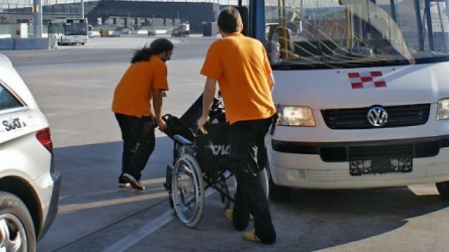 Staff assists a wheelchair user into an accessible airport shuttle bus.