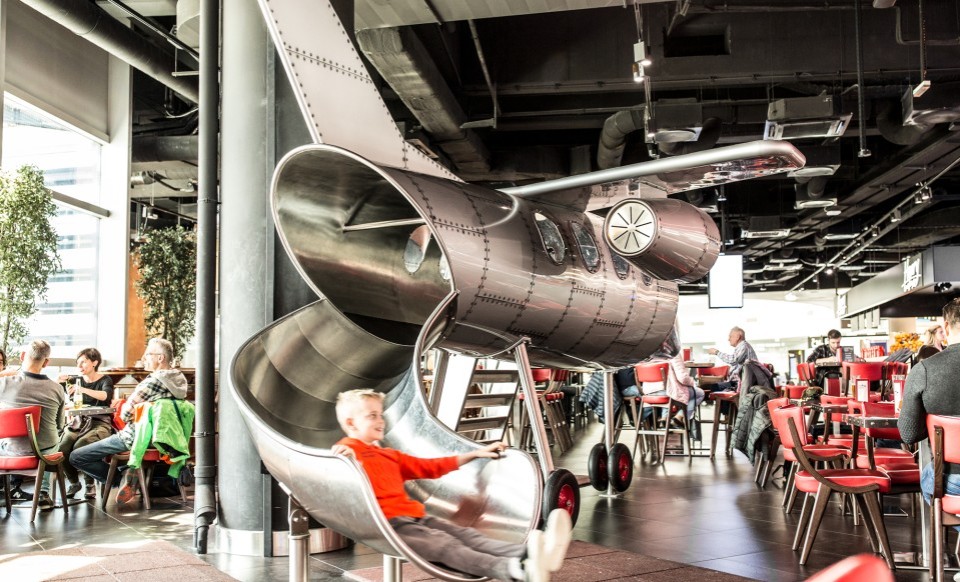 Kind rutscht aus einem Spielzeugflugzeug in einem familienfreundlichen Restaurantbereich.