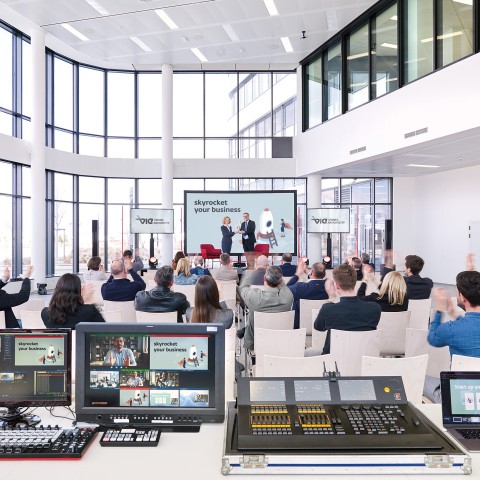Blick auf Bühne im Office Park 4. Menschen sitzen in Sesselreihen und folgen einem Vortrag.